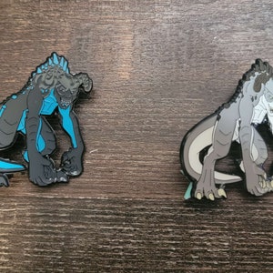 May include: Two enamel pins featuring a monster design. One pin is black and grey with blue accents, the other is grey and white. Both pins depict a creature with horns, sharp teeth, and clawed feet.