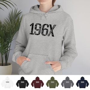 Pode incluir: Uma camisa de moletom cinza com capuz com o texto "196X GENERATION" estampado na frente. A camisa de moletom está disponível em uma variedade de cores, incluindo branco, preto, vinho, verde oliva, cinza escuro e azul marinho.
