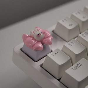 May include: A white keyboard with a pink bunny keycap. The bunny has a pink bow and white eyes.