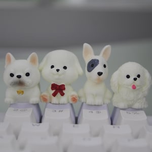 May include: Four white dog figurines with different facial expressions and details, sitting on a white keyboard with black keys. The dogs are wearing a red bow, a black collar, and have a grey patch on their eye.