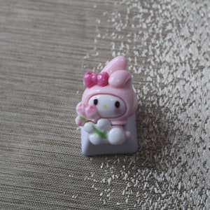 K&ouml;nnte beinhalten: Ein rosa und wei&szlig;er Keycap mit einer Comicfigur mit Hasenohren, einer rosa Schleife und einer Blume. Die Figur h&auml;lt eine Blume in der Hand.