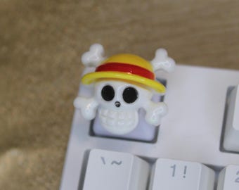 May include: A white plastic skull with a yellow and red straw hat, a keycap for a computer keyboard.