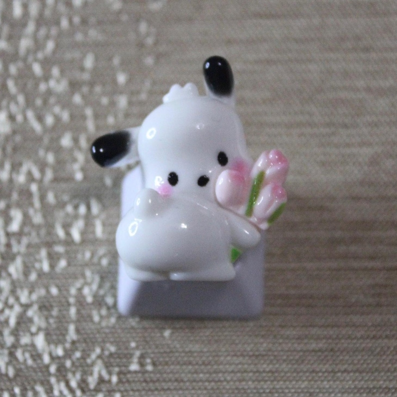 K&ouml;nnte beinhalten: Ein wei&szlig;er Keramik-Tastenkappen mit einem Comic-Tier, das einen Strau&szlig; rosa Blumen h&auml;lt. Die Tastenkappe ist f&uuml;r eine mechanische Tastatur konzipiert.