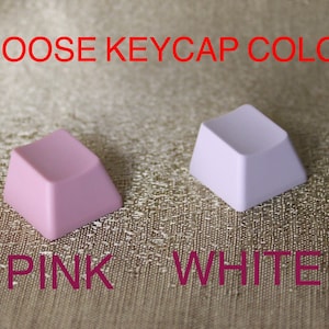 K&ouml;nnte beinhalten: Zwei Keycaps, eine rosa und eine wei&szlig;e, mit dem Text "CHOOSE KEYCAP COLOR" dar&uuml;ber und den W&ouml;rtern "PINK" und "WHITE" darunter.