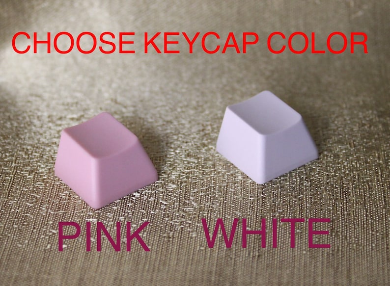 K&ouml;nnte beinhalten: Zwei Keycaps, eine rosa und eine wei&szlig;e, mit dem Text "CHOOSE KEYCAP COLOR" dar&uuml;ber und den W&ouml;rtern "PINK" und "WHITE" darunter.