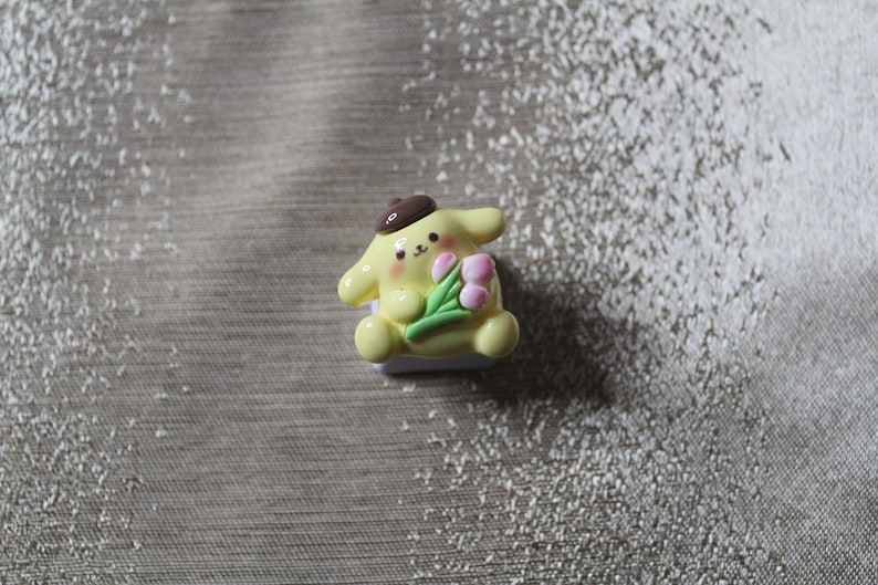 K&ouml;nnte beinhalten: Ein gelber und wei&szlig;er Keycap mit einer Comicfigur, die einen Strau&szlig; rosa Blumen h&auml;lt. Die Figur tr&auml;gt einen braunen Hut.