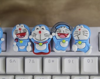 May include: Five blue and white cartoon character keycaps featuring a smiling character with a red mouth, a character with a yellow star, a character with a red bow, a character with a red bow and a character with a red mouth. The keycaps are on a white keyboard.