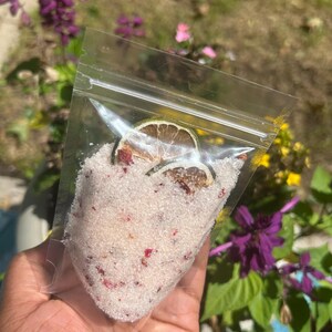 May include: A clear plastic bag filled with white bath salts with pink rose petals and dried lime slices.