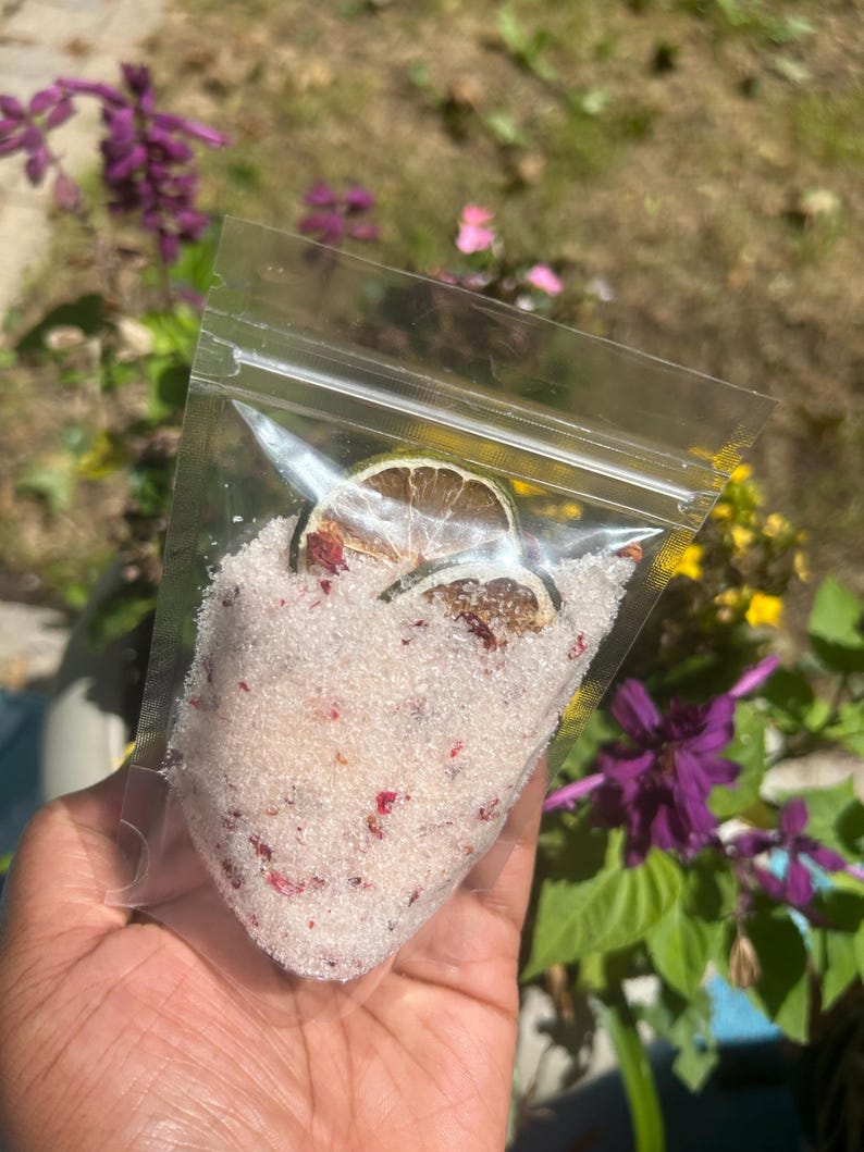 May include: A clear plastic bag filled with white bath salts with pink rose petals and dried lime slices.