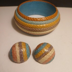 May include: A multi-colored bangle bracelet and matching earrings. The bracelet features a blue interior and is wrapped in bands of orange, blue, yellow, brown, and cream-colored snakeskin. The earrings are round and have a similar striped pattern.