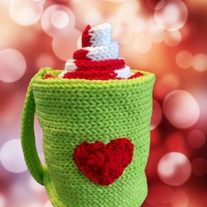 May include: A green crocheted mug with a red heart and a white and red crocheted swirl on top.
