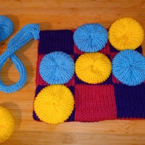May include: A knitted checkerboard game with blue and yellow circles. The board is purple and red, and there are extra blue and yellow circles off to the side.