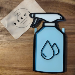 Puede incluir: Una taza de cerámica blanca con un asa negra y el texto "But First, Coffee" en negro, con una fuente de estilo manuscrito. La taza está sobre una superficie blanca.