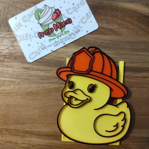 Peut inclure: Un canard jaune portant un casque de pompier orange. Le canard a des contours noirs et des yeux bruns. Une carte-cadeau avec le texte "Froyo Mama" et une image d'un yaourt glacé est en arrière-plan.