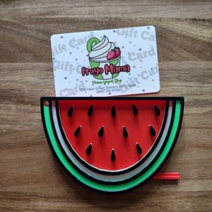 Pode incluir: Um objeto em forma de melancia com centro vermelho, sementes pretas e camadas de casca verde e branca. Acima, um cartão-presente branco para a Froyo Mama Frozen Yogurt Shop, com um gráfico de um copo de iogurte com coberturas.