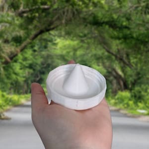 May include: White plastic bottle cap with a cone-shaped spout in the center. The cap is held in a hand.