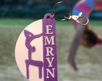 May include: Purple and pink 3D printed keychain with a gymnast silhouette and the name "EMRYN" on the side.