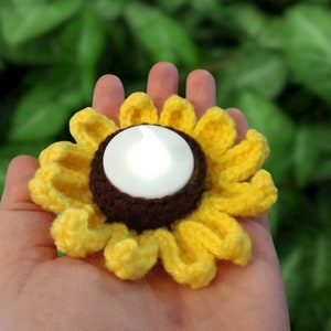 May include: A crocheted sunflower tea light holder with a white tea light inside. The holder is yellow with a brown center.
