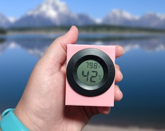Puede incluir: Un higrómetro digital rosa y negro con una pantalla que muestra 79,8 grados Fahrenheit y 42% de humedad.