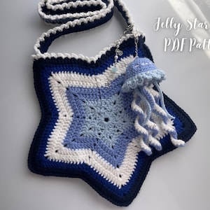 May include: A handmade, star-shaped crochet bag in shades of blue, white, and navy. The bag features a decorative jellyfish charm and the text "Jelly Star Bag PDF Pattern". The strap is white with a navy border.