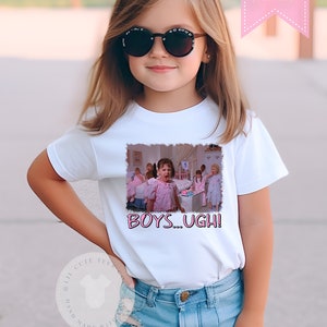 May include: A white t-shirt with a pink graphic of a girl from the movie 'Mean Girls' saying 'Boys... Ugh!'