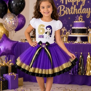 May include: A white short-sleeved shirt with a gold glitter number 6, the name Janie, and a cartoon character graphic, paired with a layered purple tulle skirt featuring gold and black ribbon trim and a matching bow at the waist and hair clip.