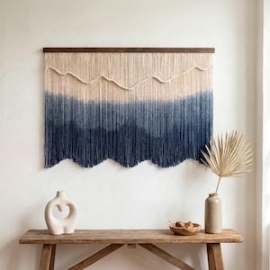 May include: A large wall hanging with a gradient design. The top section is a light beige, transitioning to a deep navy blue at the bottom. The piece is mounted on a dark brown wooden rod, creating a modern, bohemian aesthetic.