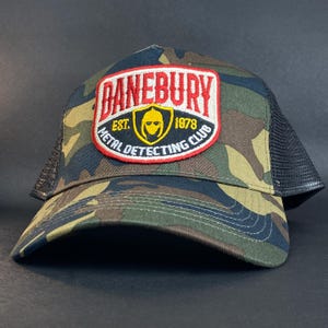 Puede incluir: Una gorra de camionero de camuflaje con una malla negra en la parte posterior. La gorra presenta un parche bordado en rojo, amarillo y blanco que dice "Banebury Est. 1978 Metal Detecting Club".