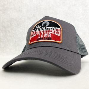 Op de afbeelding: Grijze truckercap met een zwart en rood geborduurd patch met de tekst "The Slaughtered Lamb Yorkshire".