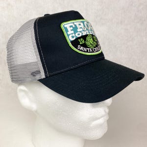 May include: Black and grey trucker hat with a green, white, and blue embroidered patch that says "Frog  Company 19 Santa Cruz".