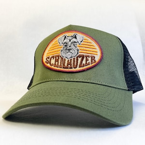 Puede incluir: Gorra de camionero Schnauzer verde oliva con la parte trasera de malla negra. La parte delantera presenta un parche bordado con una ilustración de perro Schnauzer y la palabra "SCHNAUZER" en letras marrones.