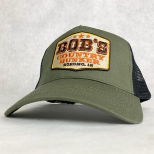 May include: A green and black trucker hat with a brown patch that says "Bob's Country Bunker Kokomo, IN" in orange and white lettering.