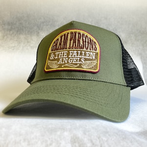 Op de afbeelding: Een groene en zwarte truckercap met een bruin en geel geborduurd patch met de tekst "Gram Parsons & The Fallen Angels".