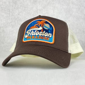 May include: A brown and white trucker hat with a patch that says "Thloston Paradise" with a palm tree and a planet design.