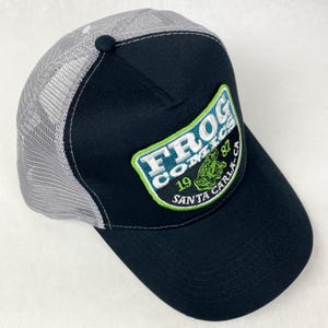 May include: Black and grey trucker hat with a green, white, and blue embroidered patch that says "Frog Comics 1987 Santa Carla CA" and a green frog illustration.