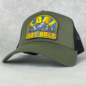 以下が含まれることがあります： 緑と黒のトラッカーハット。黄色と青のパッチには「Go Not Dole」の文字と山脈のグラフィックが描かれている。