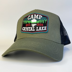 May include: A green and black trucker hat with an embroidered patch that says "Camp Crystal Lake Est. 1935".