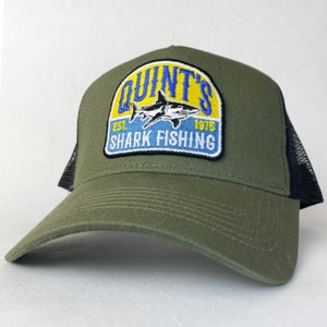 May include: A green and black trucker hat with a yellow, blue and white embroidered patch that says "Quint's Est. 1976 Shark Fishing".