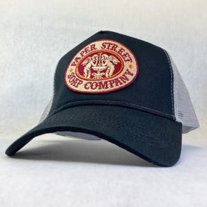 May include: Black and grey trucker hat with a red, orange and white embroidered patch that says "Paper Street Soap Company".