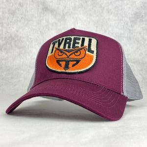 May include: Burgundy and gray trucker hat with a black and orange embroidered patch featuring an owl and the word "TYRELL".