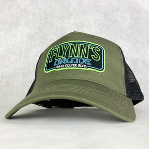 May include: A green and black trucker hat with a neon green and blue embroidered patch that says "Flynn's Arcade 9543 Culver Blvd."
