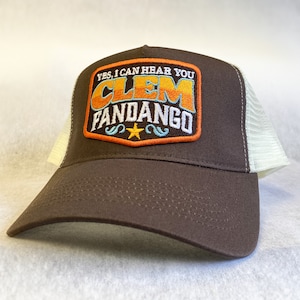 Może przedstawiać: Brązowa czapka trucker z siateczką z tyłu. Czapka ma naszywkę z haftem, na której widnieje napis "Tak, słyszę cię Clem Fandango" w retro czcionce z pomarańczowymi, niebieskimi i żółtymi akcentami.
