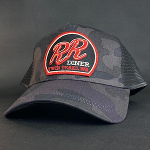 Puede incluir: Gorra de camionero de camuflaje negro y gris con la parte trasera de malla negra. La parte delantera presenta un parche circular con el texto "RR DINER TWIN PEAKS, WA" en rojo y blanco.