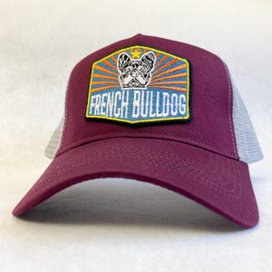 May include: Burgundy and grey trucker hat with a patch featuring a French Bulldog and the text "French Bulldog".