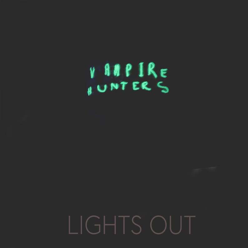 May include: A black background with the words "Vampire Hunters" written in green glow-in-the-dark paint. Below the words is the text "Lights Out" in white.