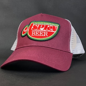 May include: A burgundy baseball cap with a white mesh back. The front of the cap features a patch with the words "Aspen Beer" in white lettering, outlined in green and red.