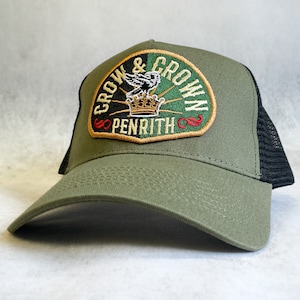 Puede incluir: Una gorra de camionero verde y negra con un gran parche bordado que dice "Grow & Crown Penrith" en letras doradas, blancas y rojas. El parche presenta un pájaro negro con una corona en la cabeza.