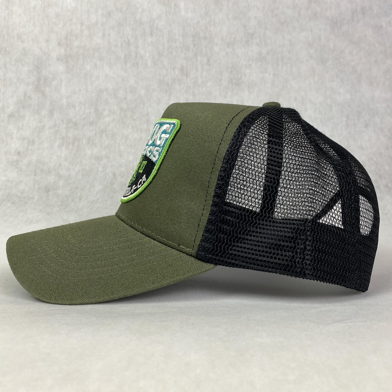 May include: A green and black trucker hat with a green and white embroidered patch that says "Big Sur" on the front. The hat has a black mesh back.