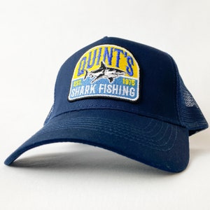 May include: A navy blue trucker hat with a yellow, blue and white patch that says "Quint's Shark Fishing Est. 1975".