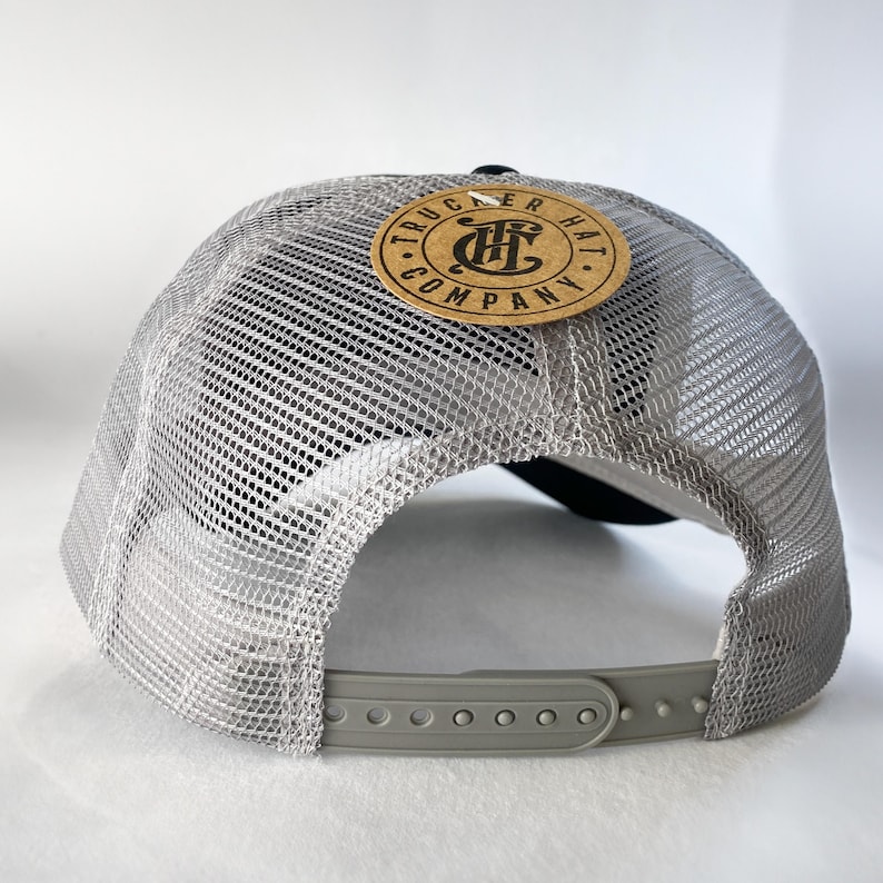 May include: A gray and black trucker hat with a brown patch that says "Trucker Hat Company" with a logo of a stylized "TH" inside a circle.